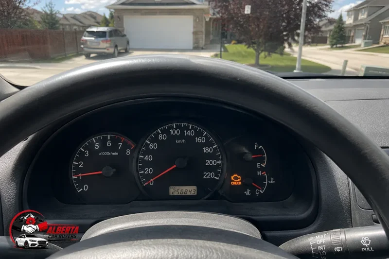 Dashboard with check engine light illuminated and 255,843 km odometer in a parked car on a sunny suburban Alberta street.